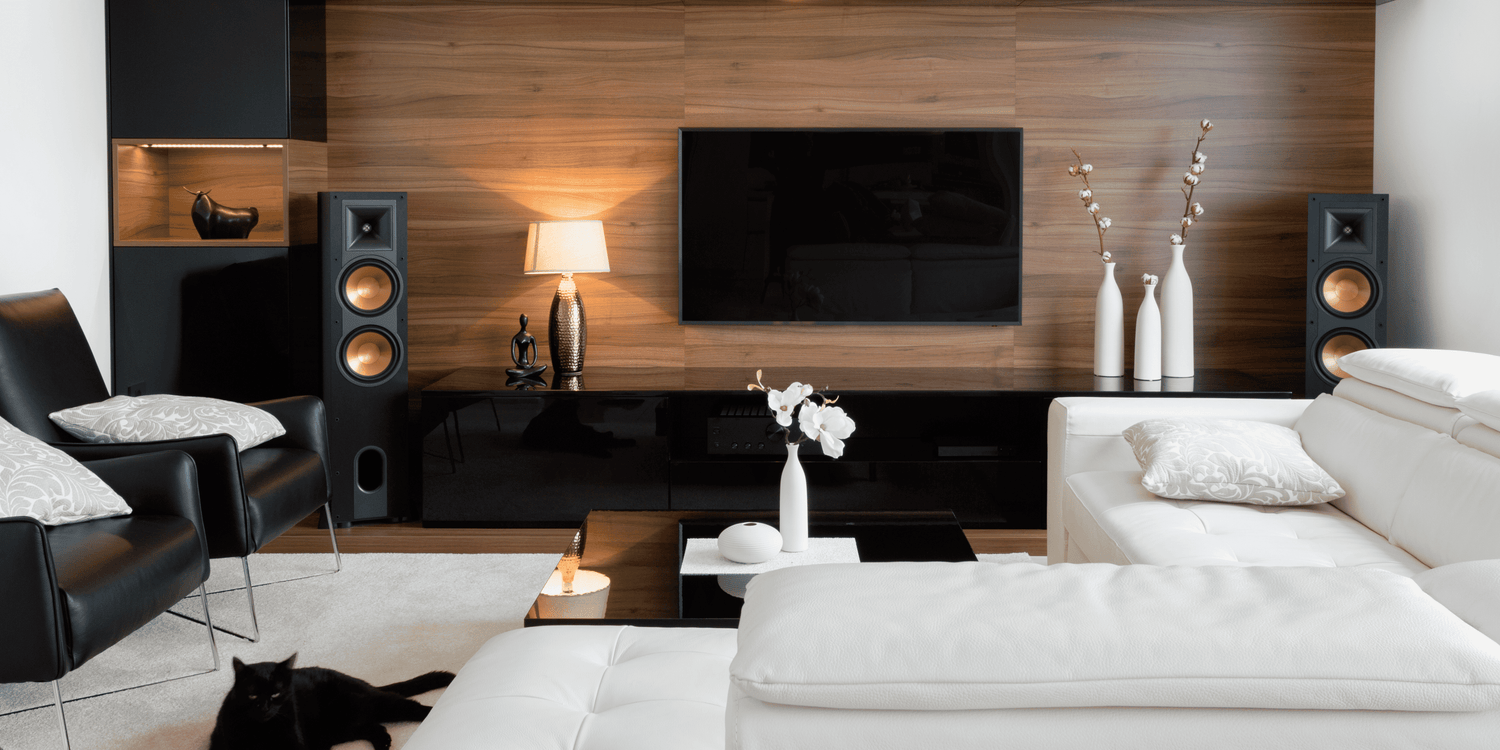 Modern living room with black sofa, white armchair, and a television on a wooden wall.